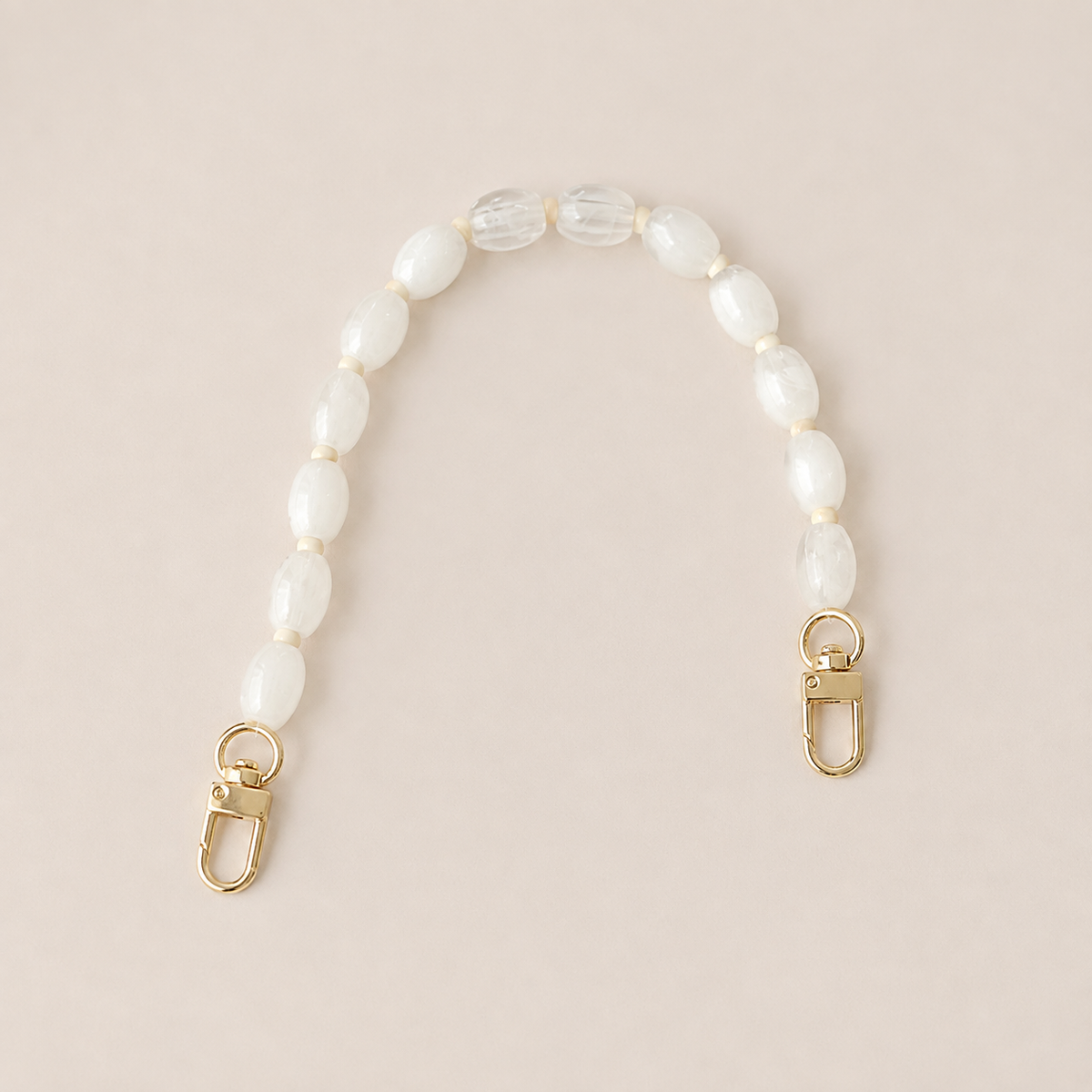 Folie à Trois Fennel short wholesale phone chain in white oval beads with cream spacers and gold clasps, laid flat on a cream background.