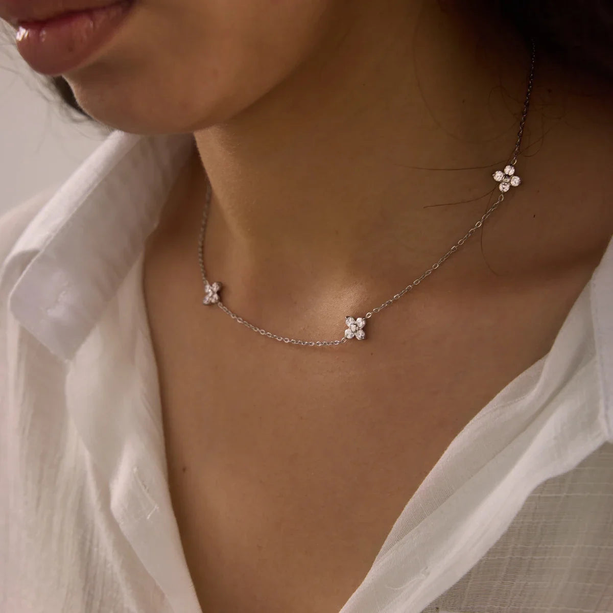Fiore NECKLACE with delicate zirconia flower stations worn with an open white shirt — Folie à Trois wholesale jewelry