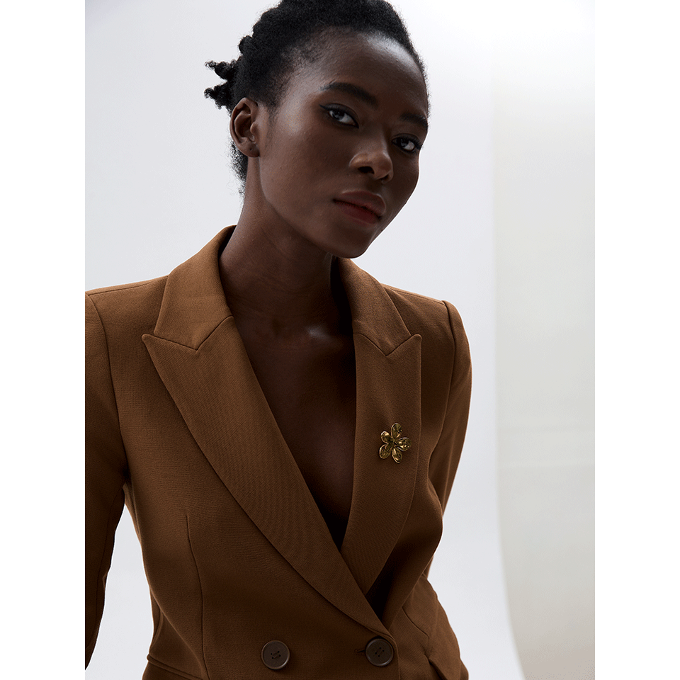 Model wears a gold Flora BROOCH pinned to the lapel of a brown blazer — Folie à Trois