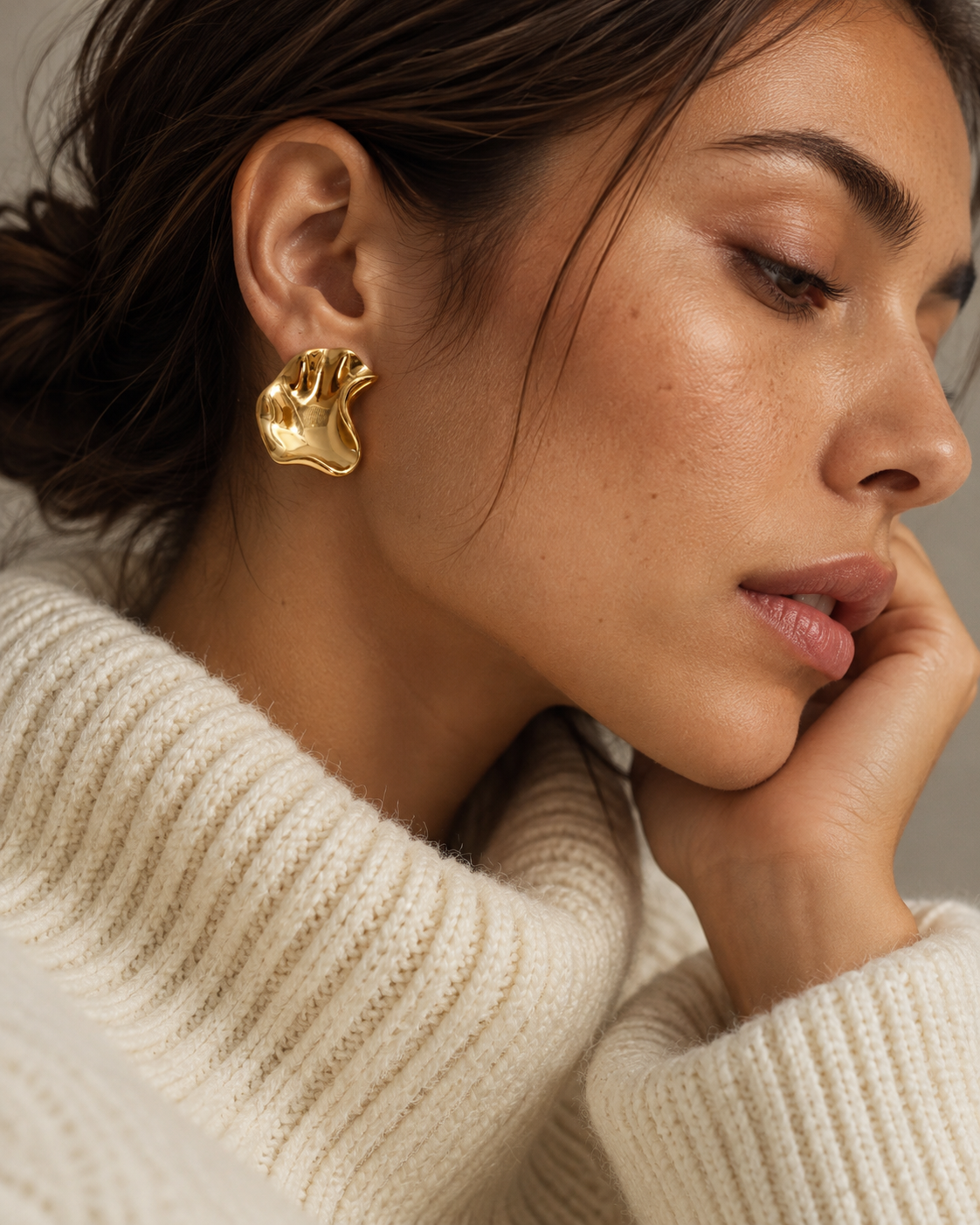 Gold Fondu EARRINGS with a wavy molten-metal finish worn by a woman in a cream ribbed turtleneck — Folie à Trois