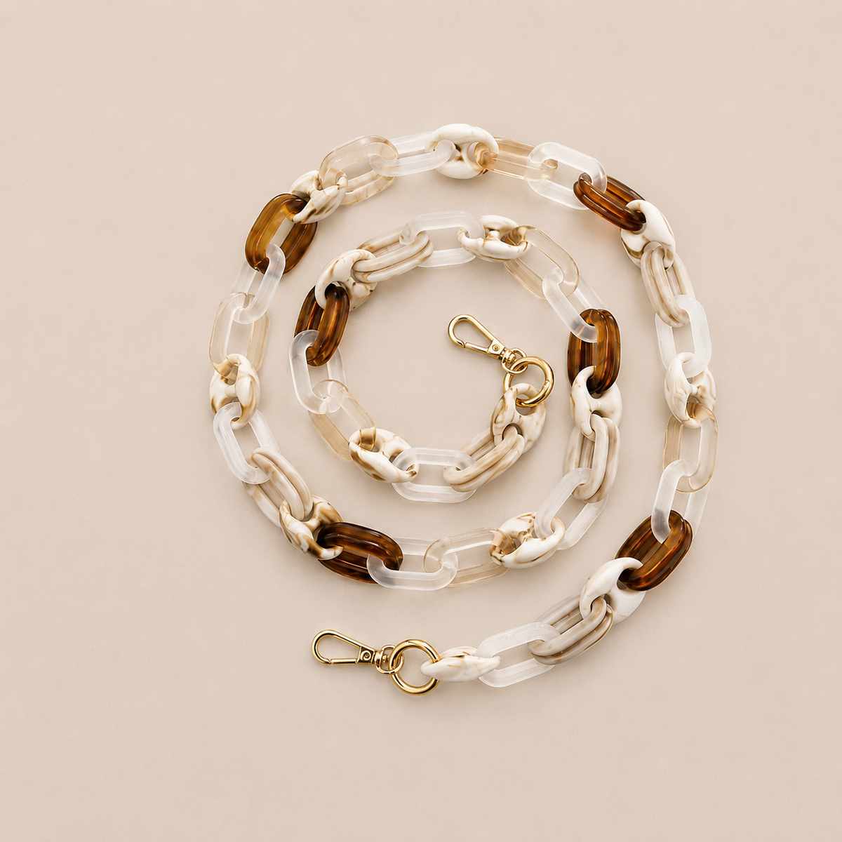 Folie à Trois Frost long phone chain in clear, white and tortoiseshell brown links with gold clasps, coiled on a cream background.