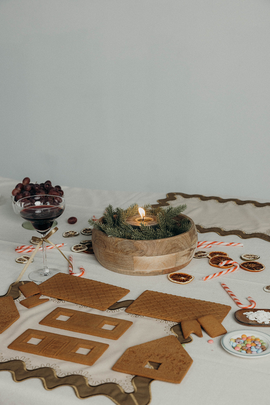 Festive tablescape with wine, a candle, and gingerbread pieces styled beside the olive Gisèle Scallop placemat with embroidered edging.