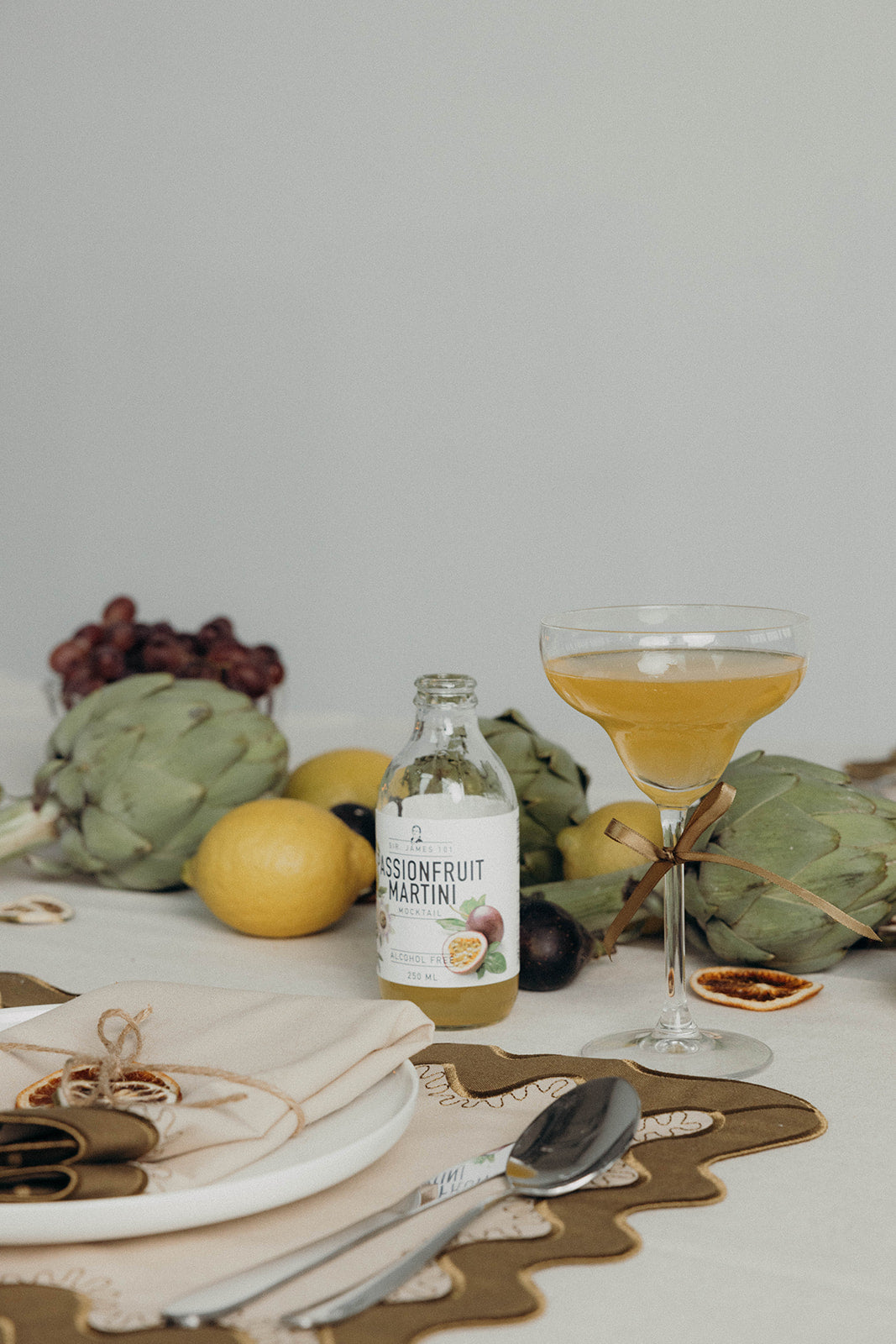 Passionfruit martini cocktail and citrus garnish styled on the olive Gisèle Scallop placemat beside a twine-tied linen napkin.