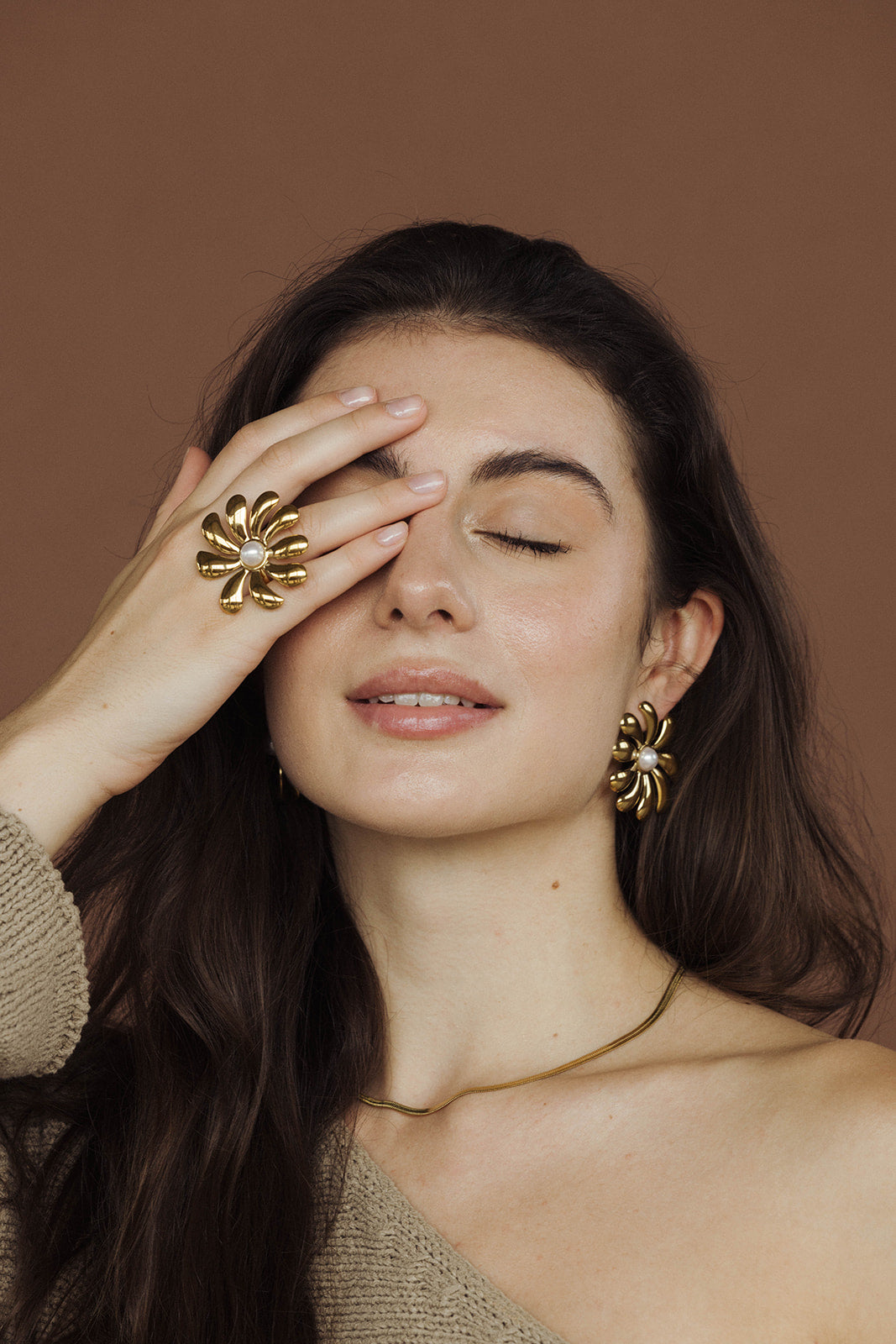 Close-up of a woman covering one eye with her hand, wearing the gold spiral-flower Glistening Embrace RING and matching earrings.