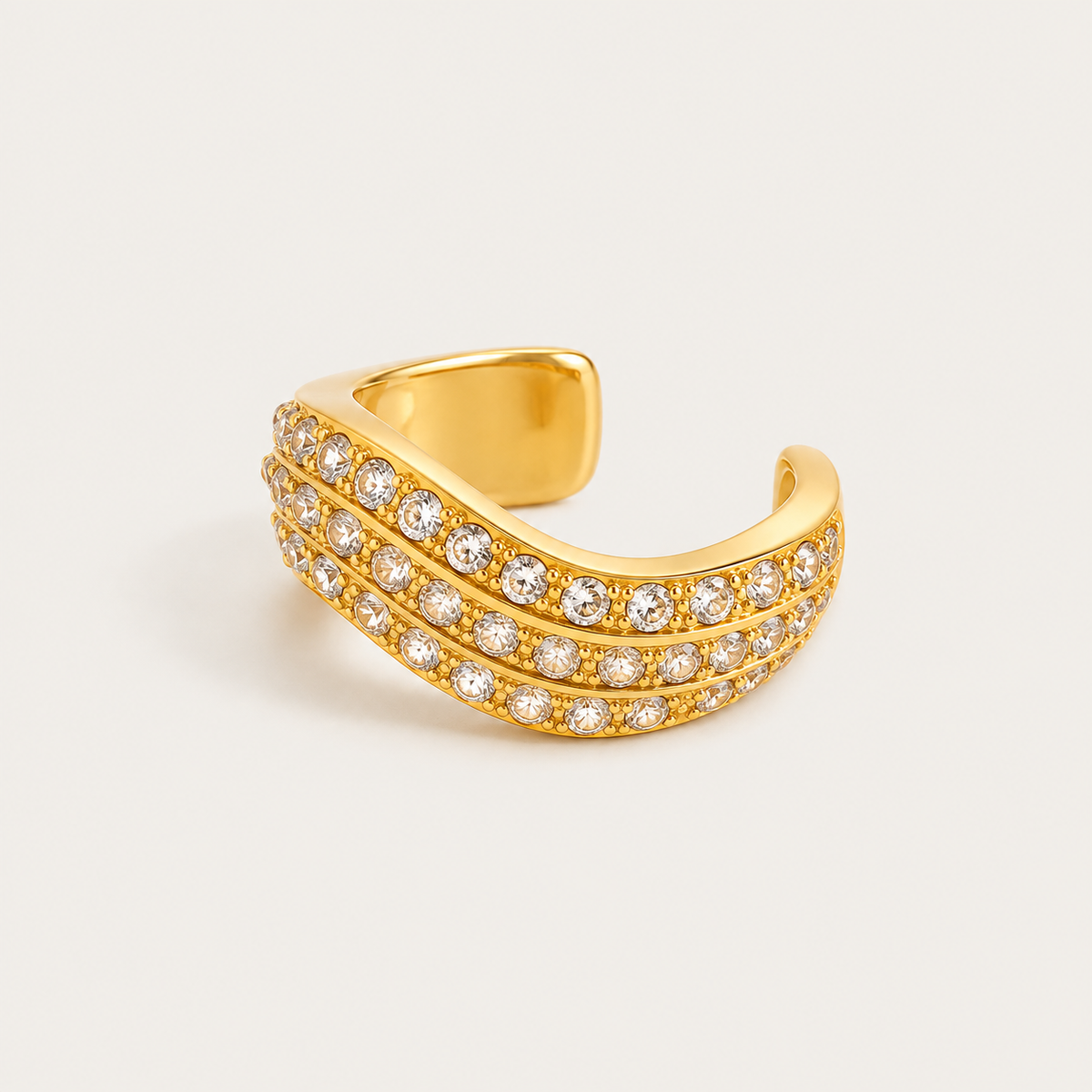 Gold wavy ear cuff set with three rows of sparkling zirconia pavé on a cream background — Folie à Trois jewelry