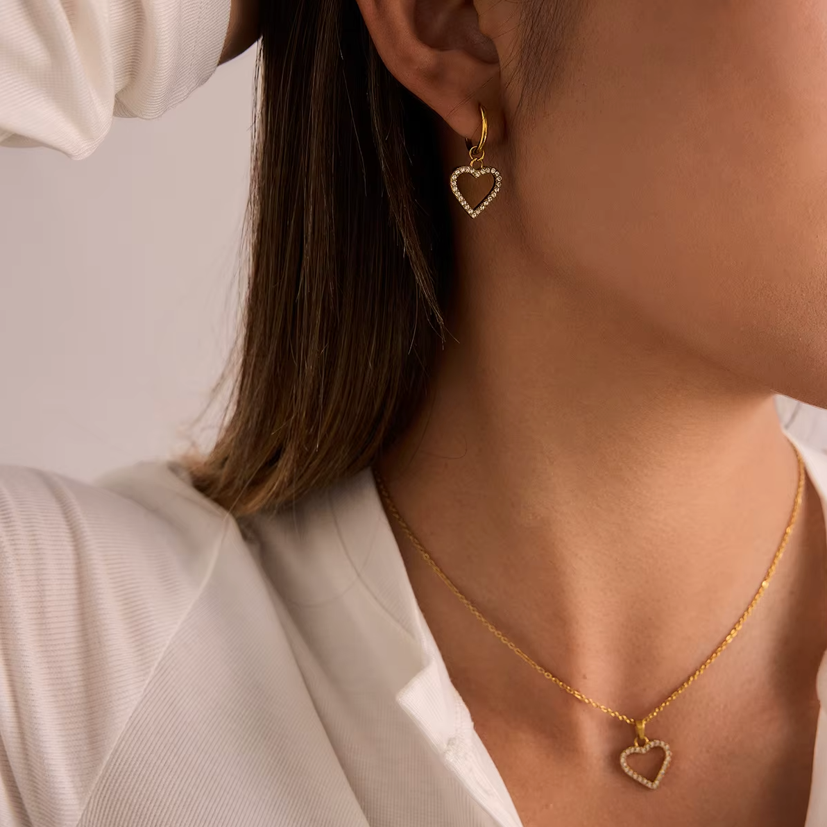 The Golden Heart NECKLACE worn alongside a matching pave heart earring, both pieces catching the light at the neckline.