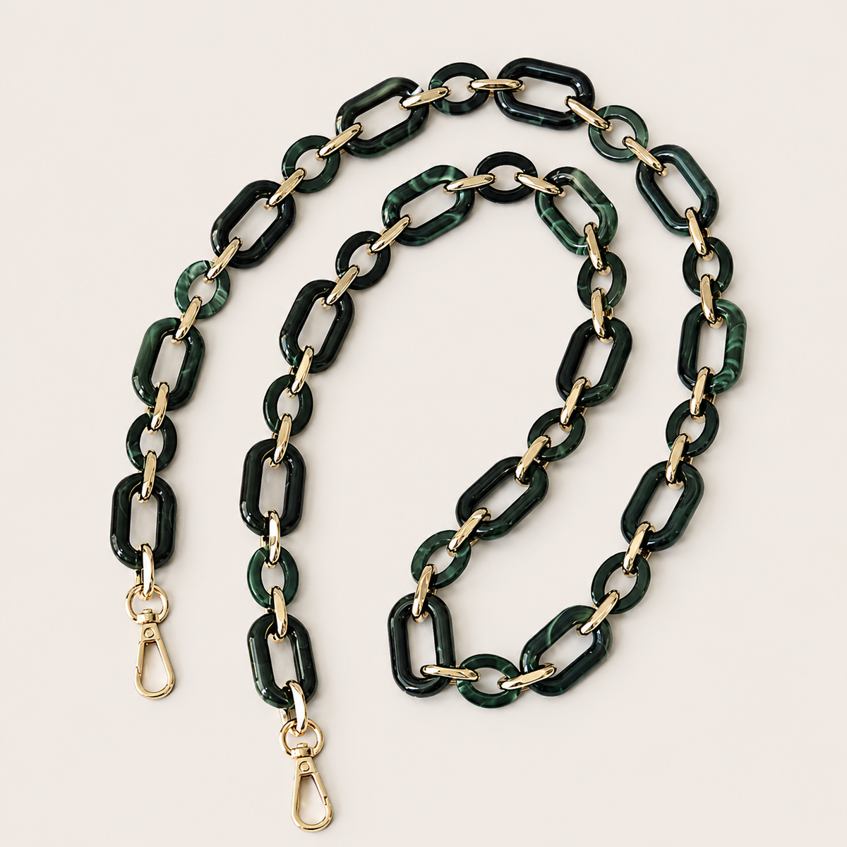 The Hazel LONG PHONE CHAIN in deep green marbled rectangular-link acrylic with gold-tone lobster clasp ends, coiled on a beige background.