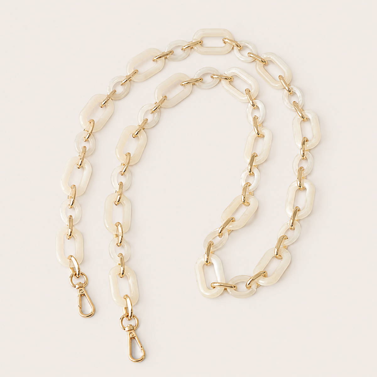 The Hazel LONG PHONE CHAIN in pearlescent ivory rectangular-link acrylic with gold-tone lobster clasp ends, coiled on a beige background.