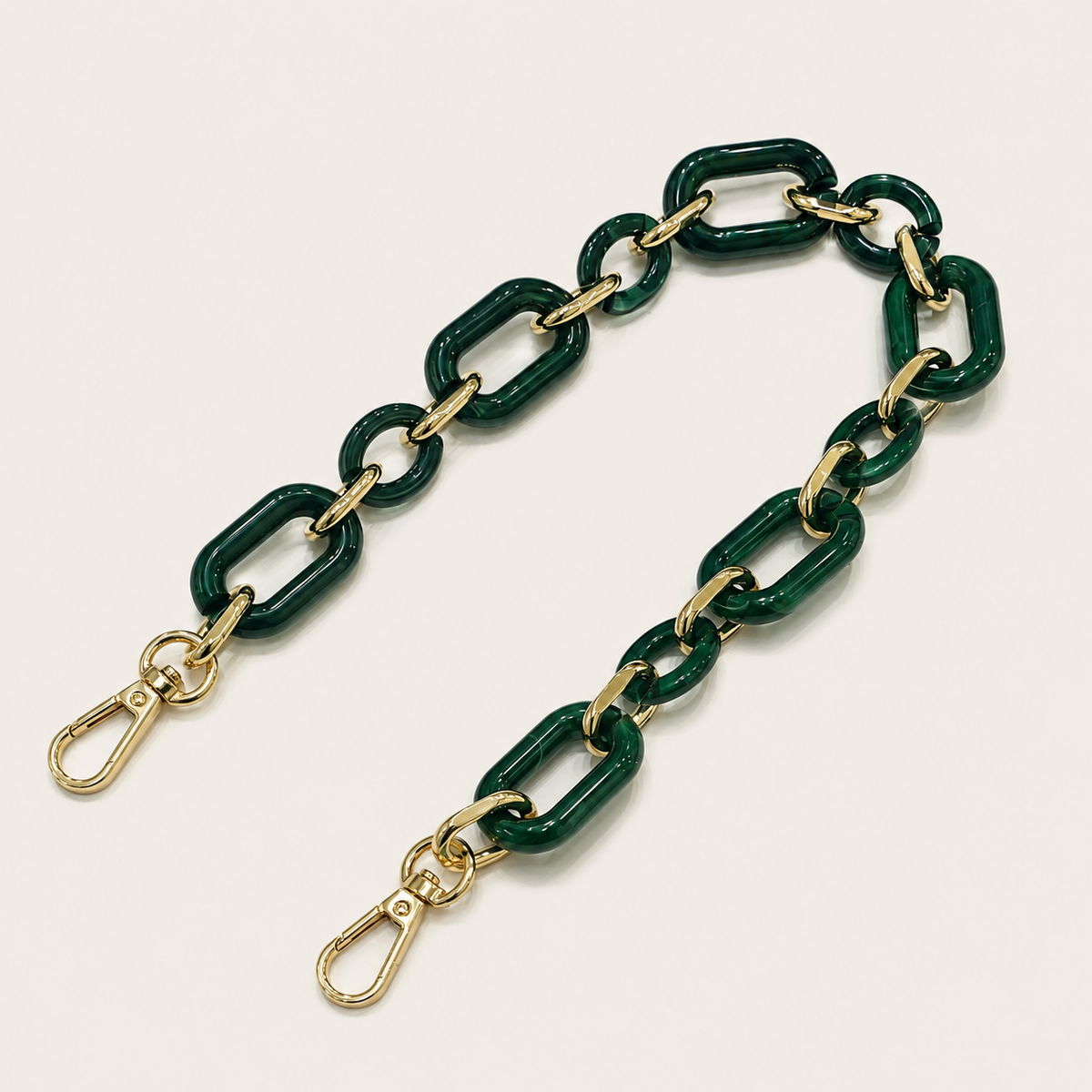 The Hazel SHORT PHONE CHAIN in deep green rectangular-link acrylic with gold-tone lobster clasp ends, fanned on a light beige background.