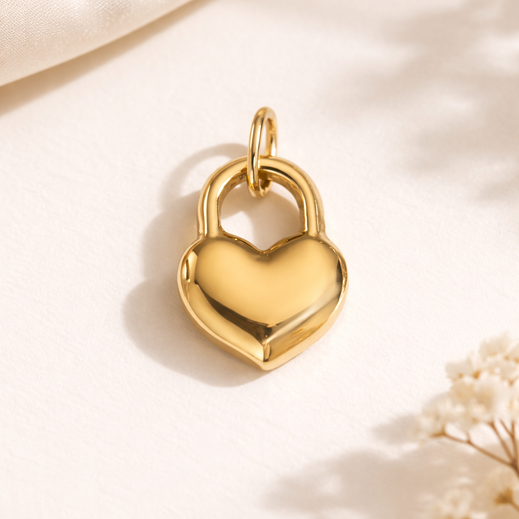 The Heart Locket CHARM in gold, styled beside sheer fabric and dried baby's breath for a soft, feminine close-up shot.