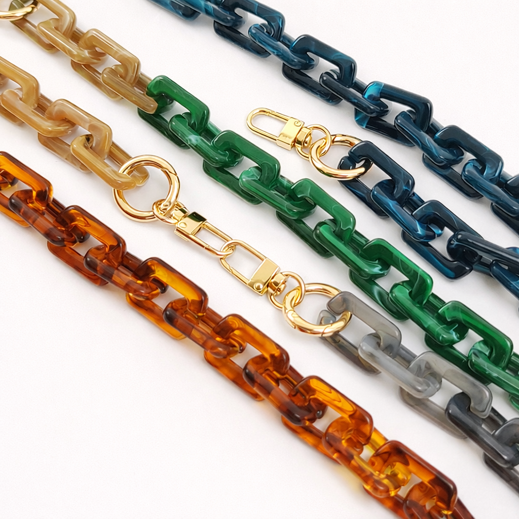 Five acrylic paperclip-link phone chains in cream, navy, green, tortoiseshell, and grey, laid out together with gold clasps.