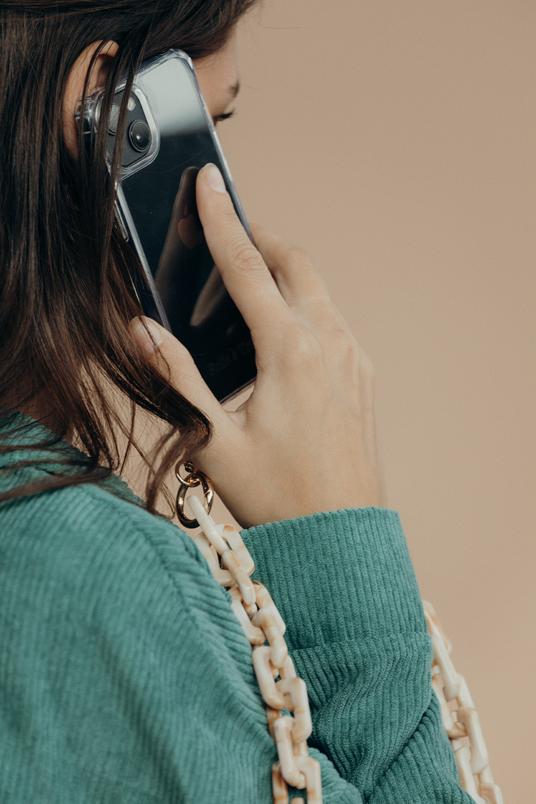 Close-up of a woman on the phone, with a cream marbled acrylic phone chain looped over her teal corduroy sleeve.