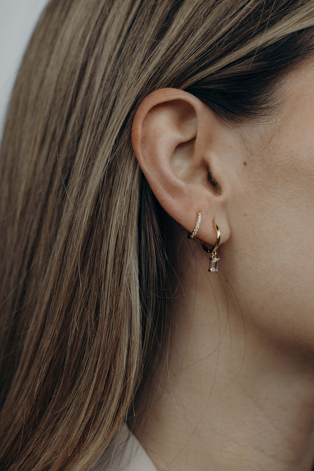 In a Dream Earrings worn on the ear, a pave hoop paired with a dangling baguette crystal charm at the lobe.