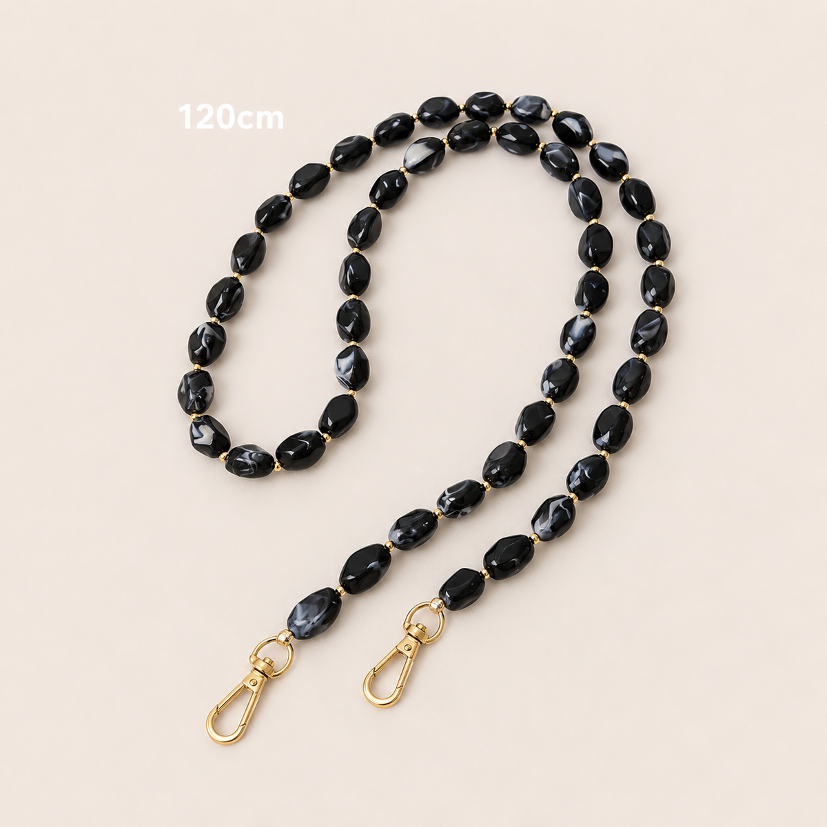 Folie à Trois Isolde long phone chain in black marbled beads with gold accent beads and gold clasps, laid flat on a cream background.