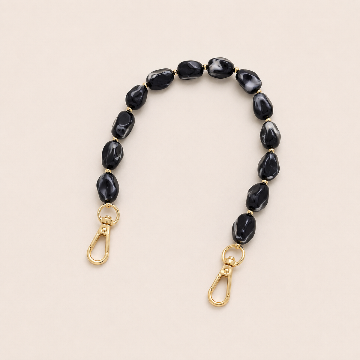 Folie à Trois Isolde short phone chain in black marbled beads with gold accent beads and gold clasps, laid flat on a cream background.