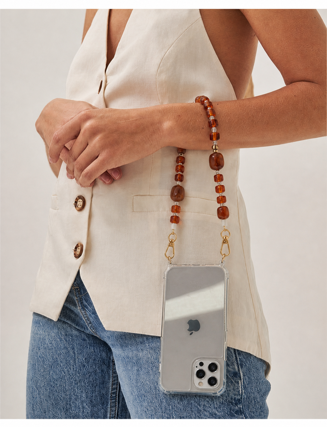 A model wears the Jaqueline SHORT PHONE STRAP in amber beads on her phone case, paired with a matching bracelet and cream blazer.