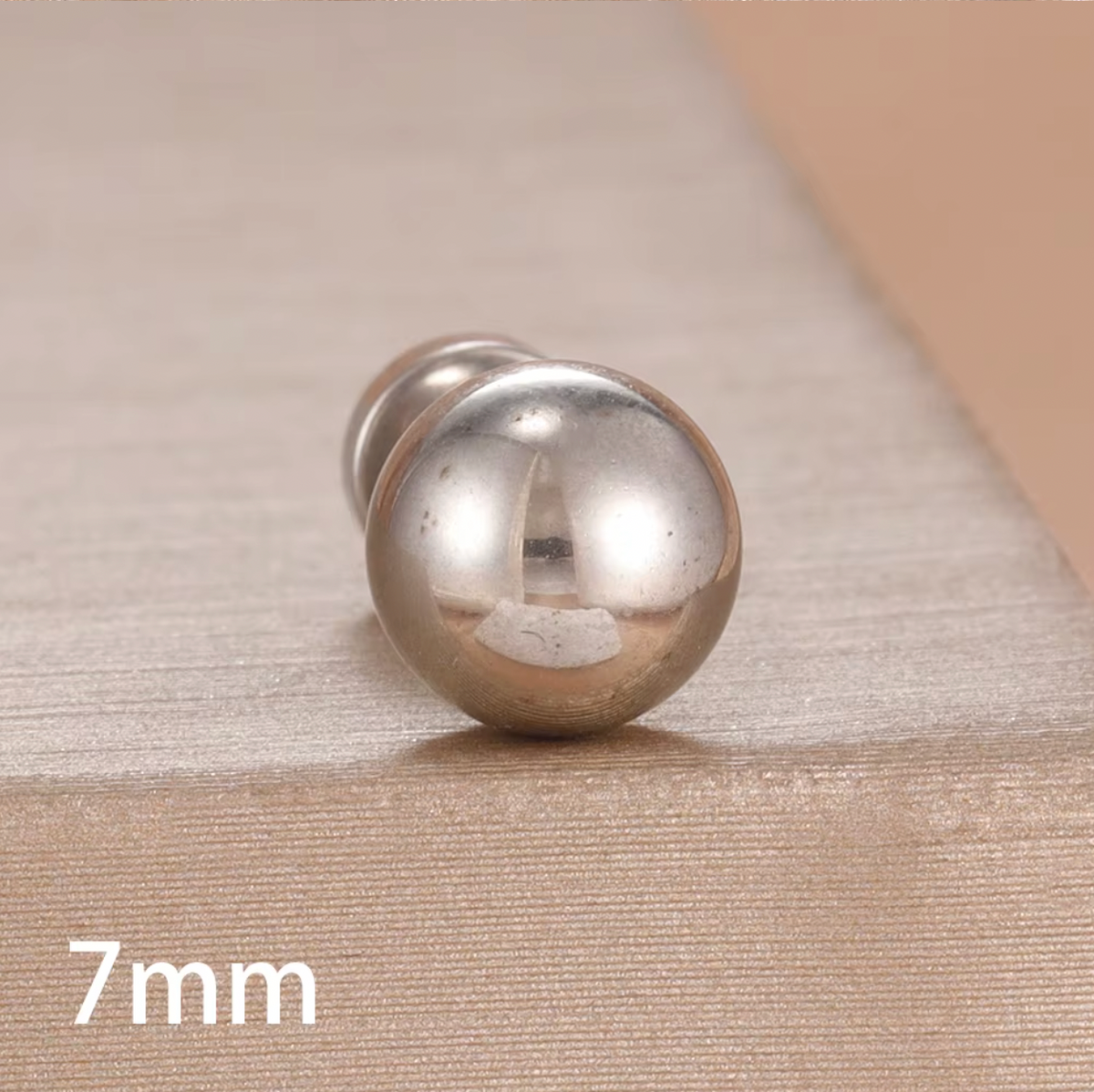 The Jean PIERCING in silver, a single 7mm labret stud shown in close-up on a textured tan surface.