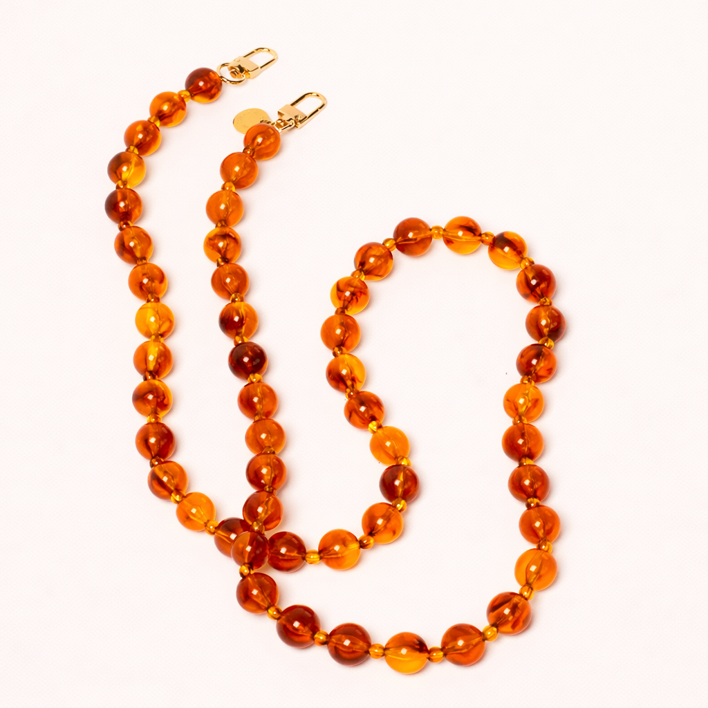 A coiled amber bead phone chain with gold clasps, shown flat on a cream background.