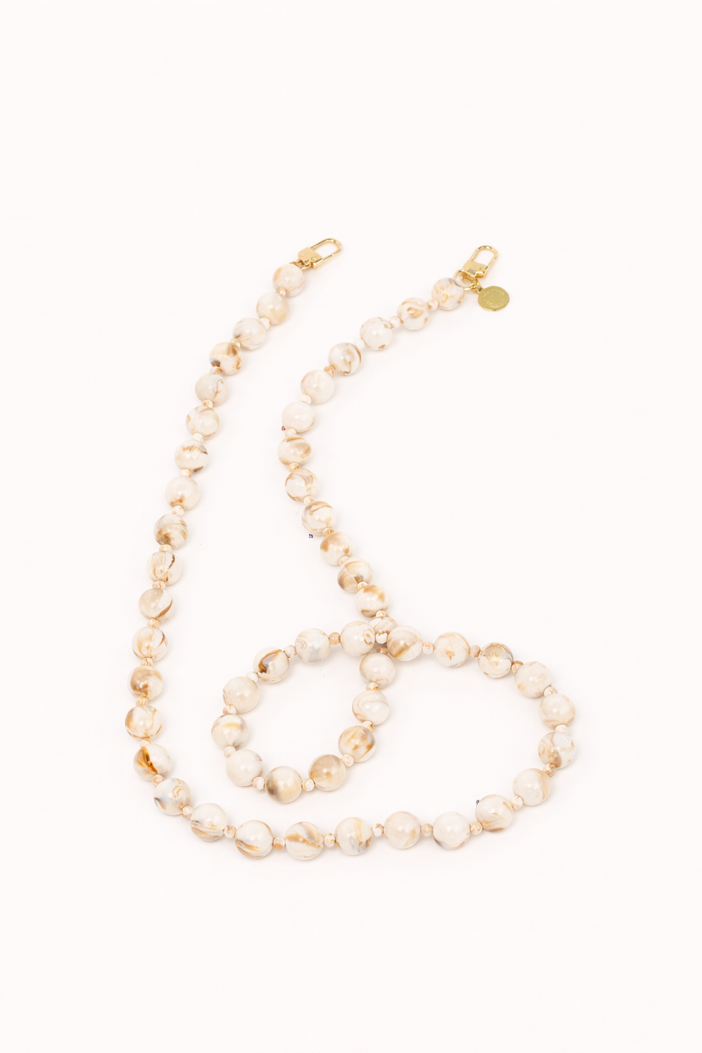 A coiled cream and gold marbled bead phone chain with gold clasps, shown on a cream background.