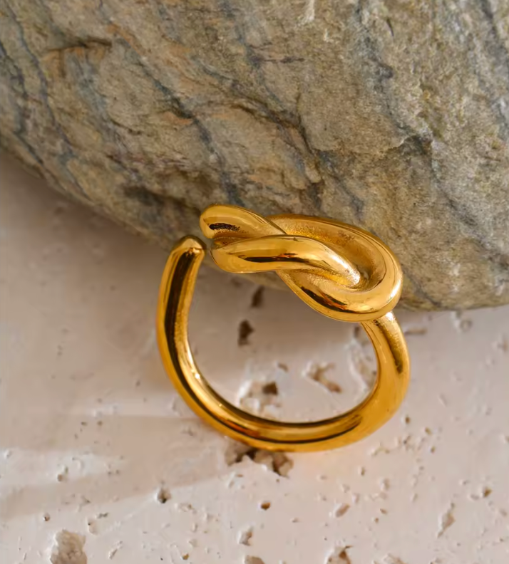 Gold Knotted RING with its open band and sculpted knot propped against a textured stone surface.