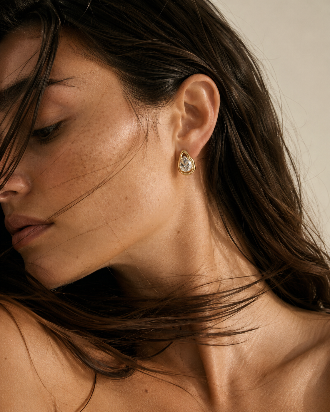 Close-up of a model with tousled hair wearing the gold Larme EARRINGS, a teardrop stud set with a pear-cut white zirconia.