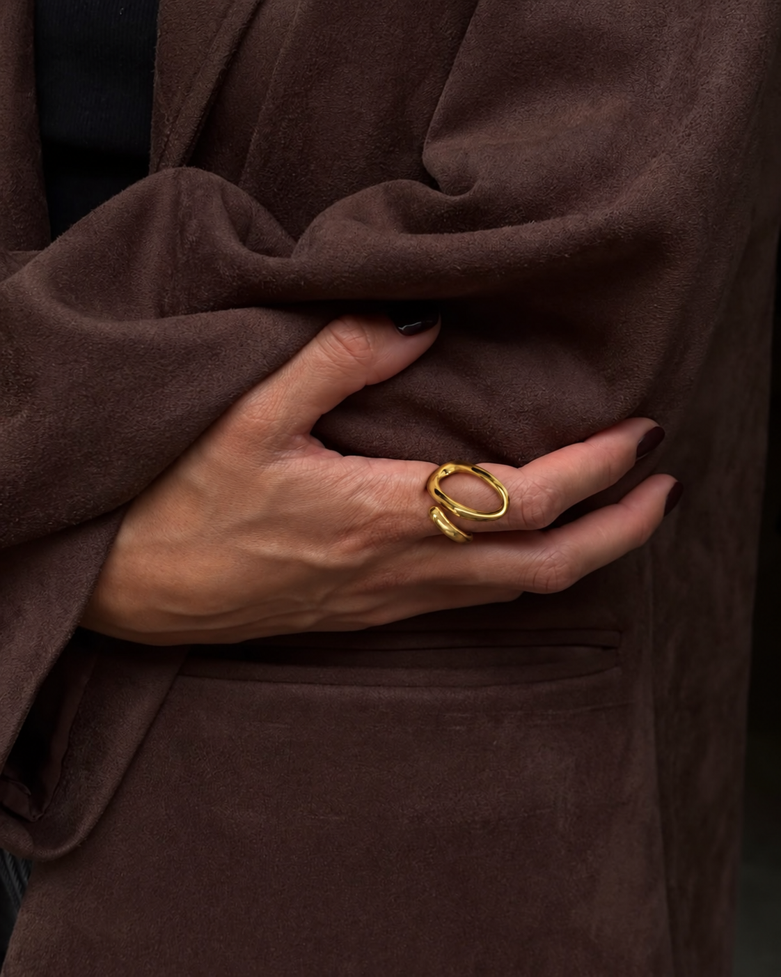 Hand resting on a brown suede jacket wears the gold Lasso RING, a slim wire looping into an open oval — Folie à Trois wholesale