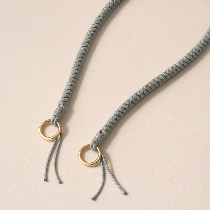 Solid gray braided Layover long phone strap, close-up of the knotted gold ring and fringe end.