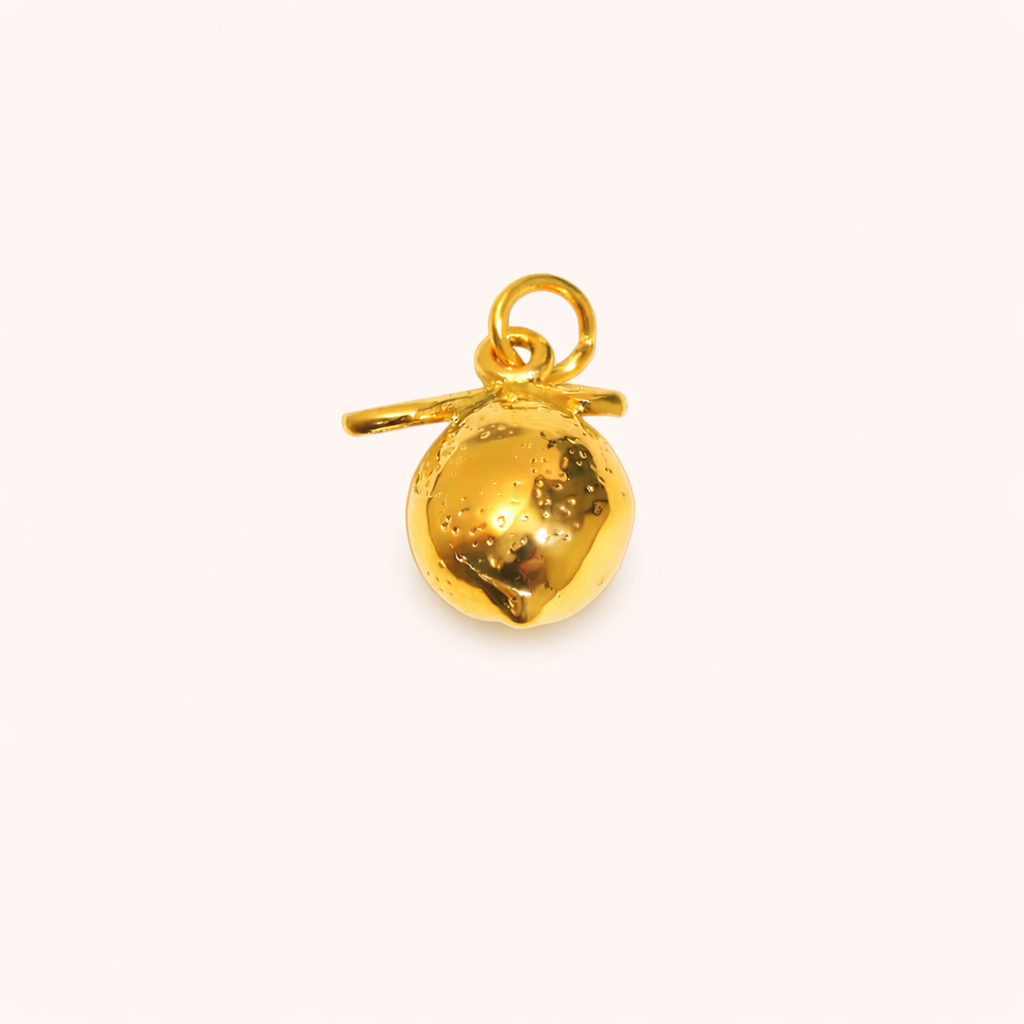 The Lemon CHARM in a studio flat lay, a polished gold pendant with a dimpled lemon texture and small stem on a cream background.