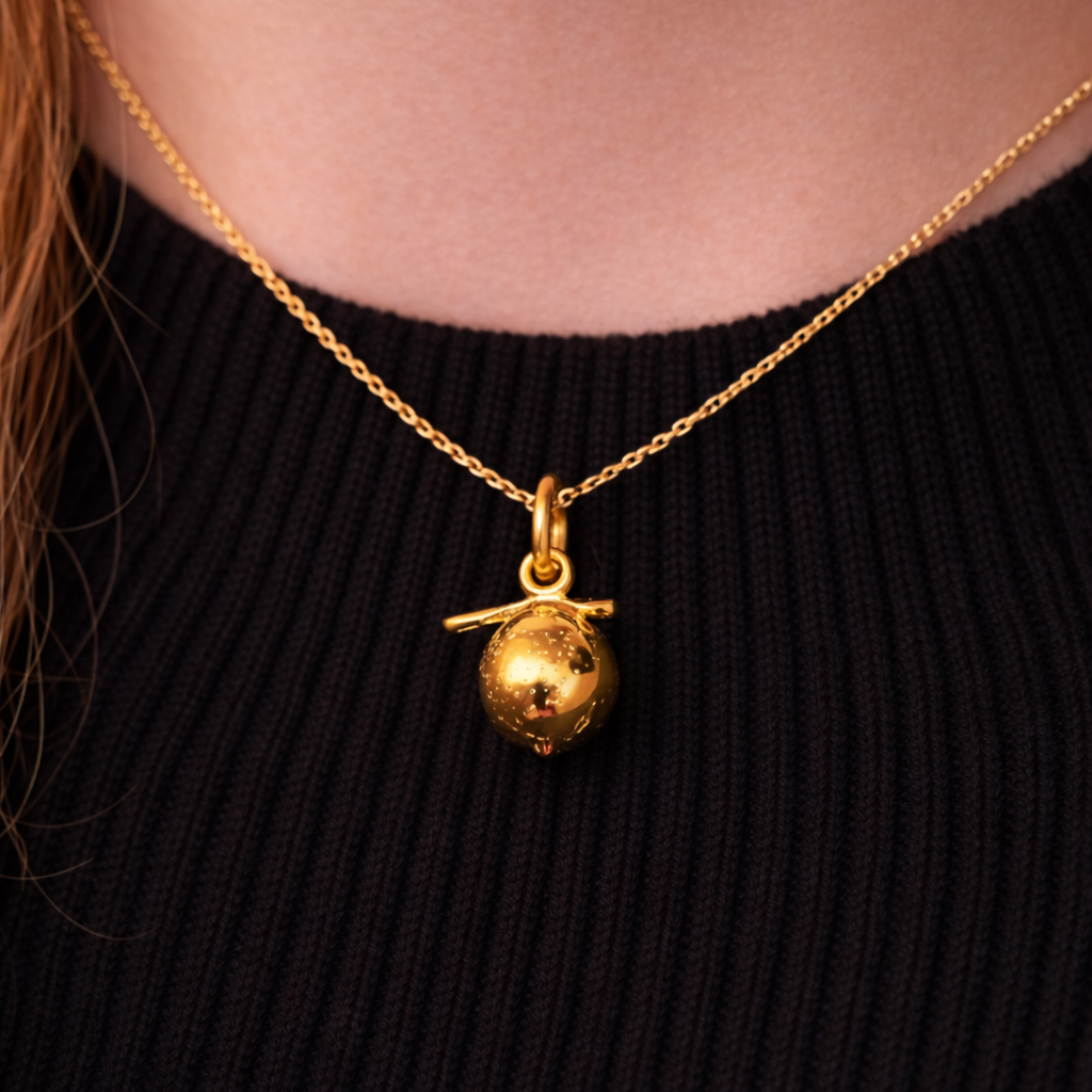 The Lemon CHARM worn at the neckline, a polished gold lemon pendant on a fine gold chain against a black ribbed sweater.