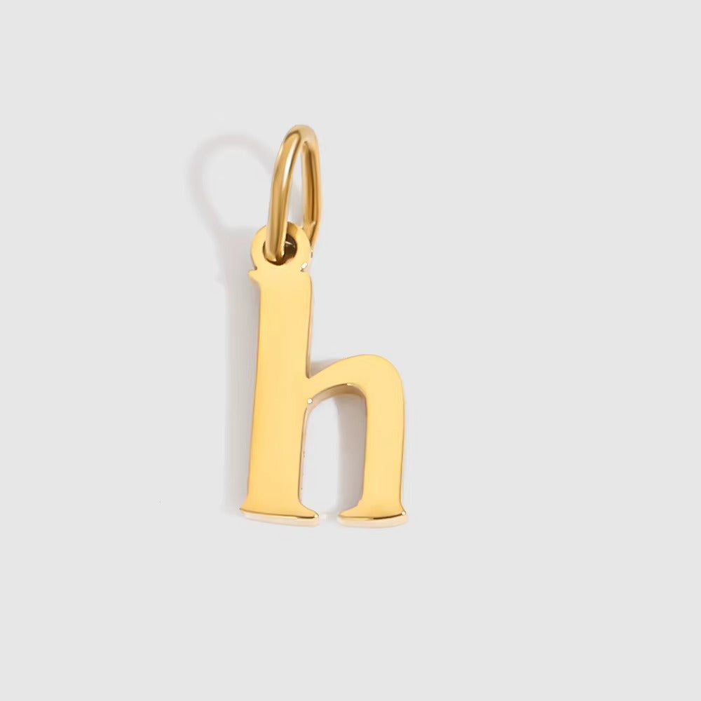 The Letter CHARM in lowercase h, a polished gold pendant in a serif h shape, shown in close-up on a light grey background.