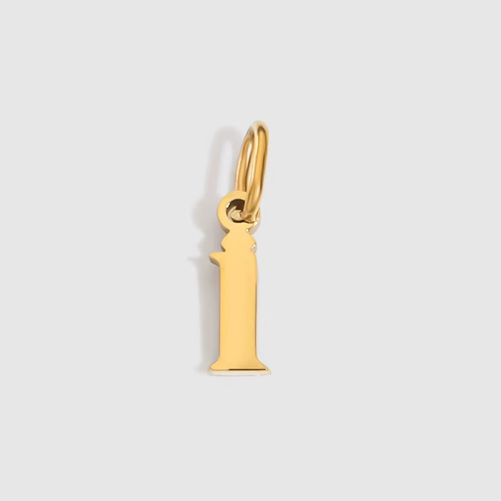 The Letter CHARM in lowercase i, a polished gold pendant in a serif i shape, shown in close-up on a light grey background.