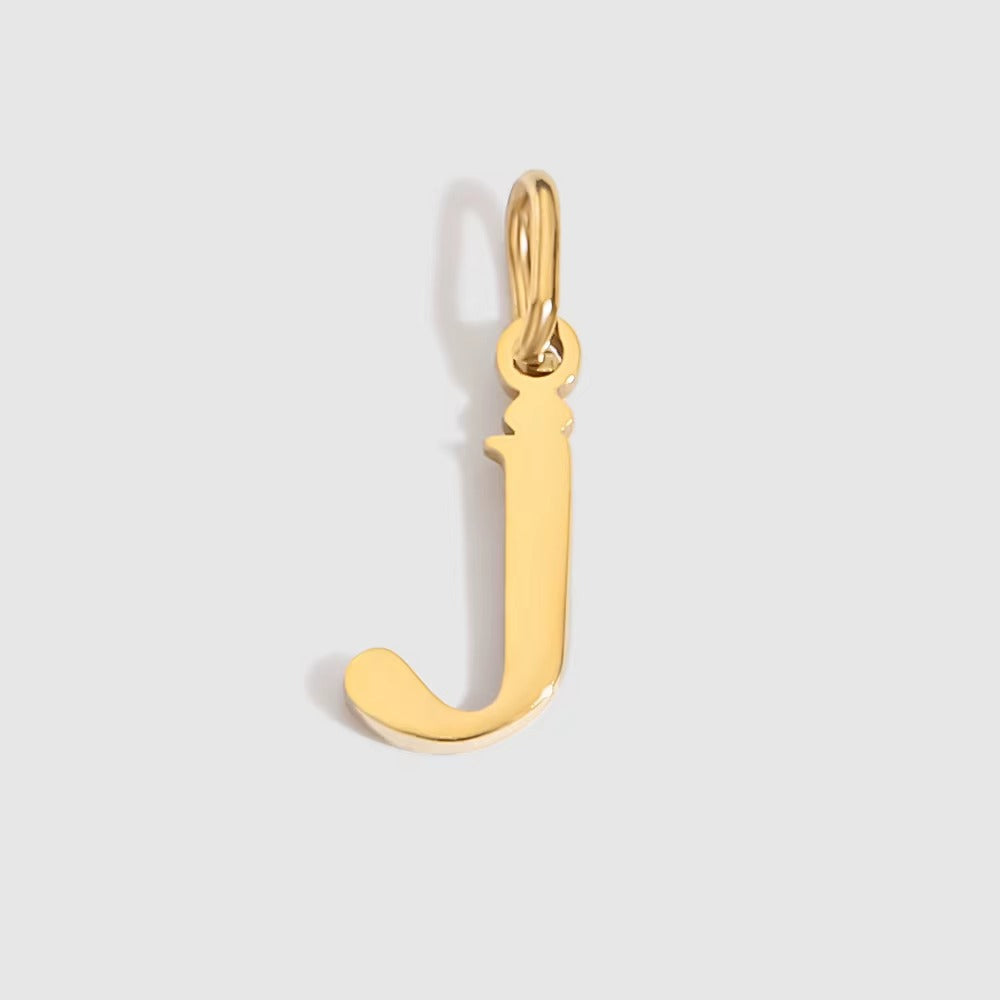 The Letter CHARM in lowercase j, a polished gold pendant in a serif j shape, shown in close-up on a light grey background.