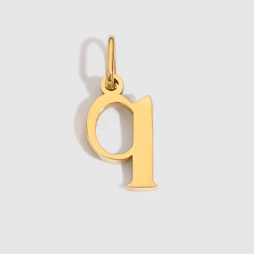 The Letter CHARM in lowercase q, a polished gold pendant in a serif q shape, shown in close-up on a light grey background.