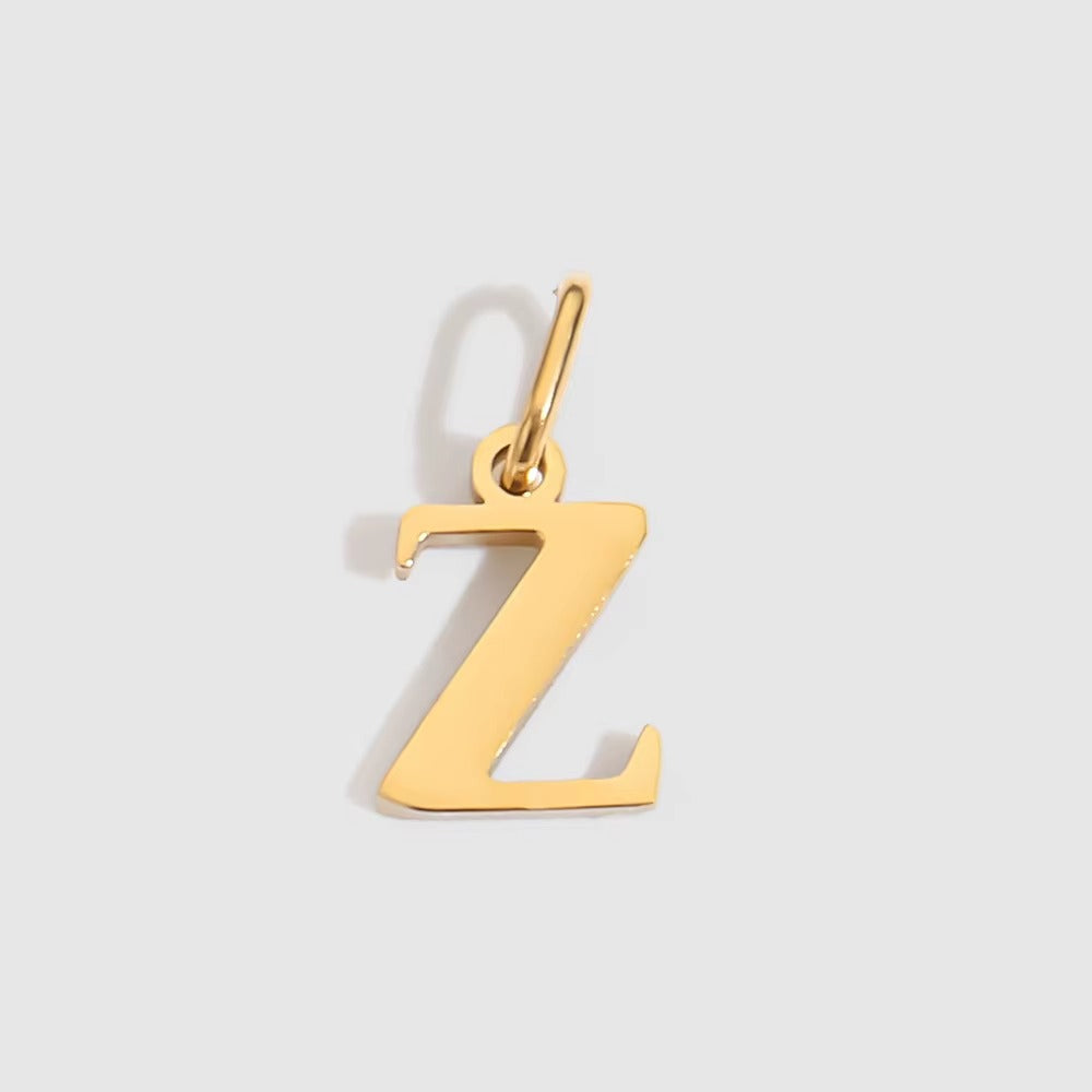 The Letter CHARM in lowercase z, a polished gold pendant in a serif z shape, shown in close-up on a light grey background.