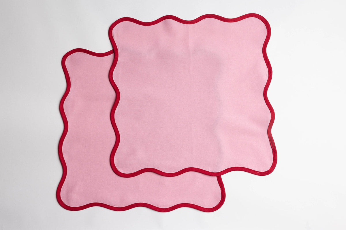 Two pink Lilou Scallop napkins with red scalloped trim laid flat and overlapping against a plain white background.