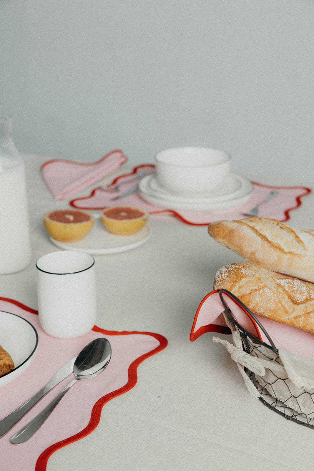 Pink Lilou Scallop napkins dress a breakfast table set with grapefruit halves, a milk bottle, mug and baguettes.