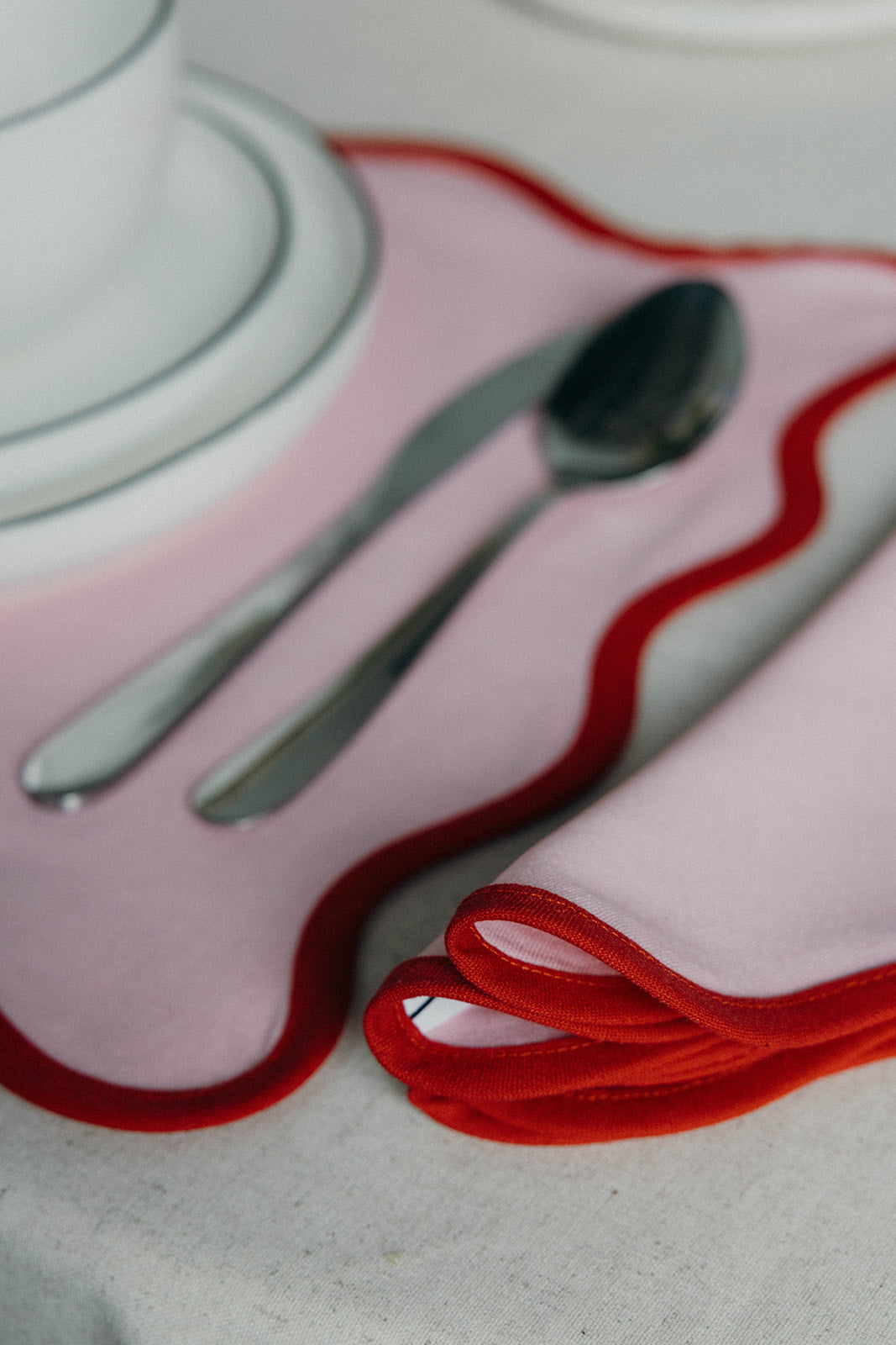 Pink Lilou Scallop napkin folded beside cutlery and a white plate on its matching scalloped placemat.