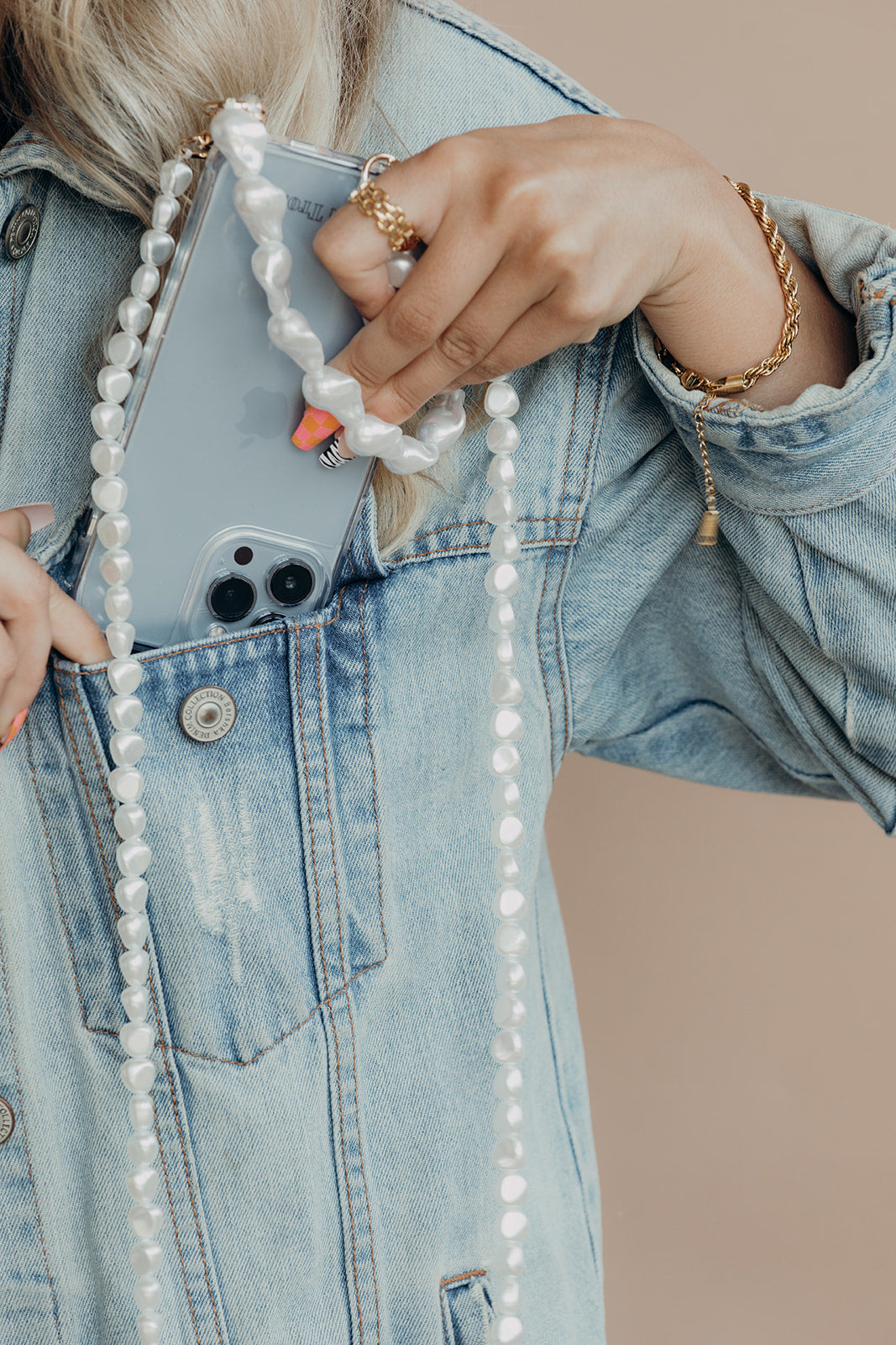 Woman in a denim jacket slipping her phone into her pocket, the white pearl phone cord from the pearl PHONE STRAP BUNDLE hanging down.