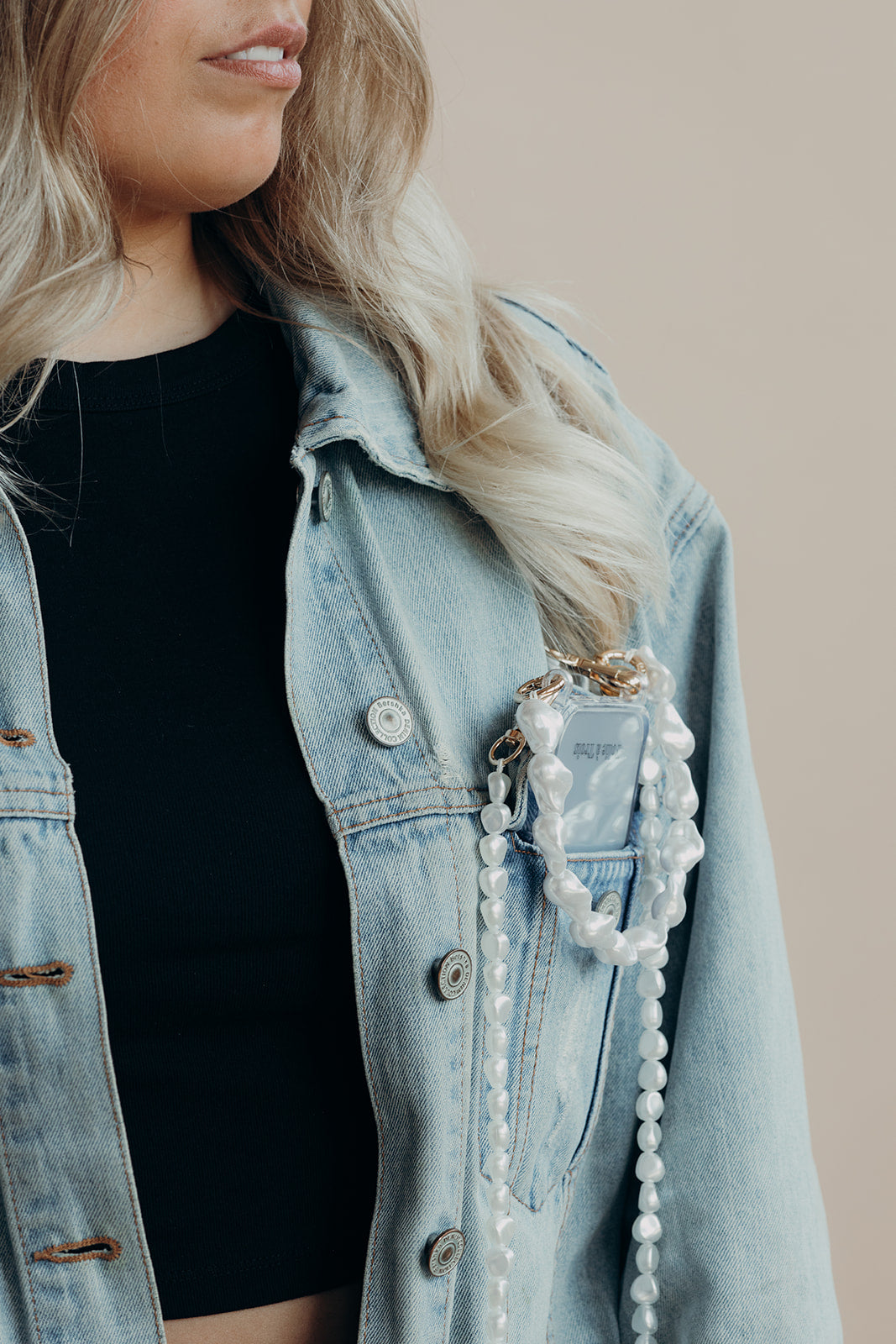 Long Pearl Phone Cord in white baroque pearls clipped to a phone in a denim jacket pocket, worn over a black top.