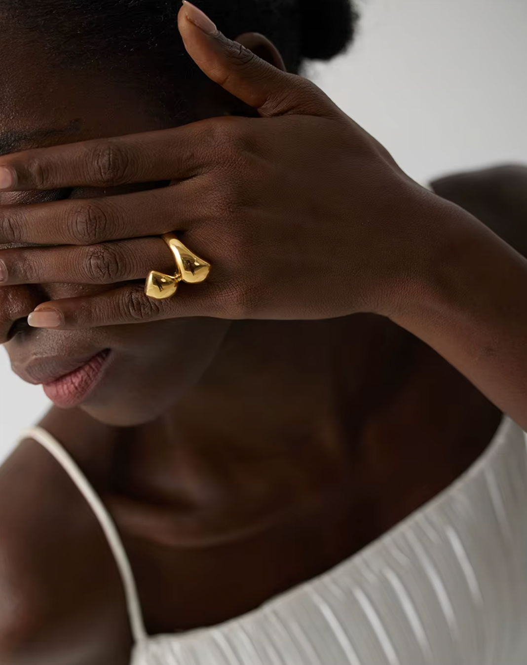 Model covers her eyes with a hand wearing the gold Lunaire RING's two overlapping domes on her finger.