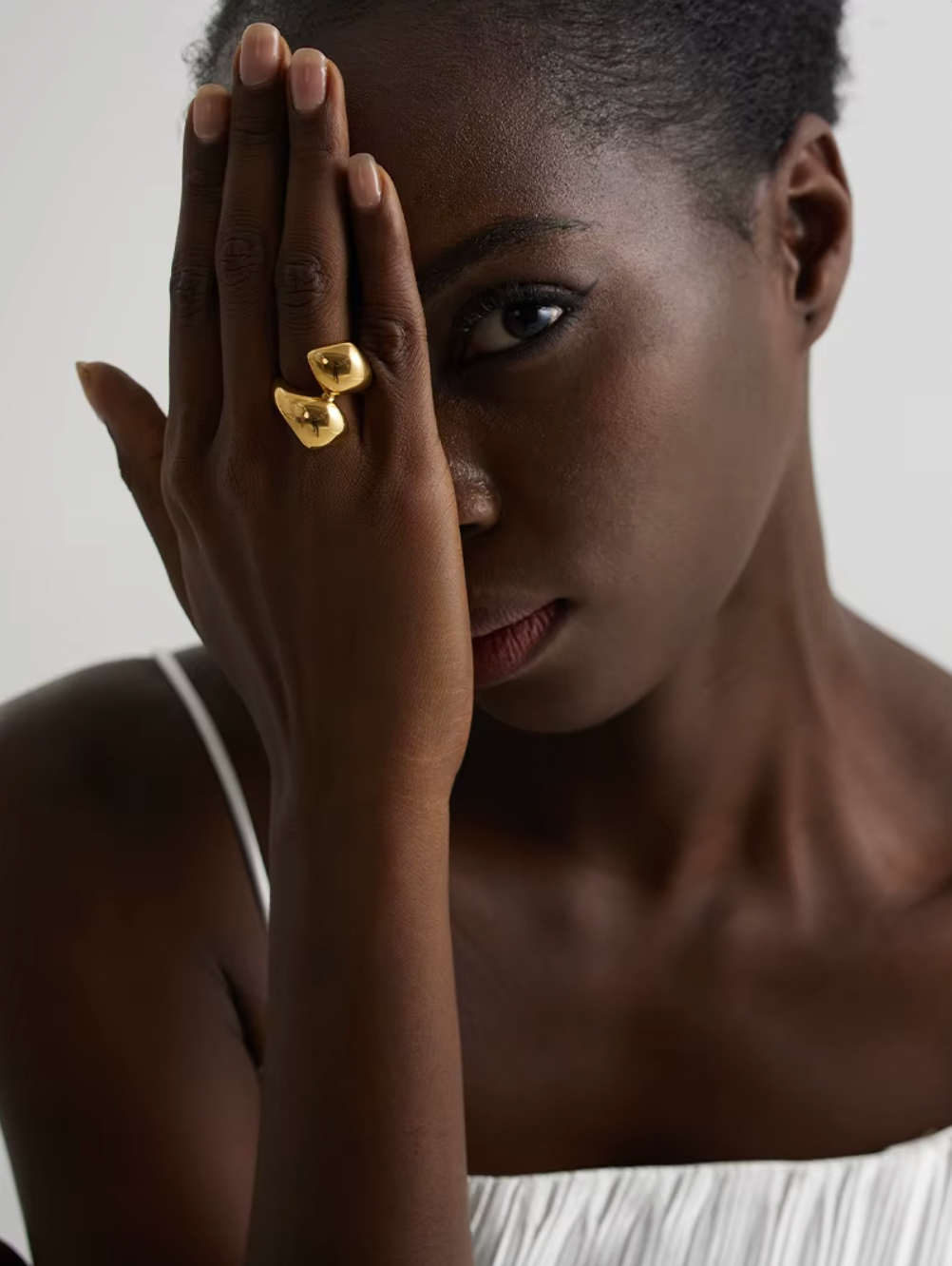 Model covers half her face with a hand wearing the gold Lunaire RING's two overlapping domes.