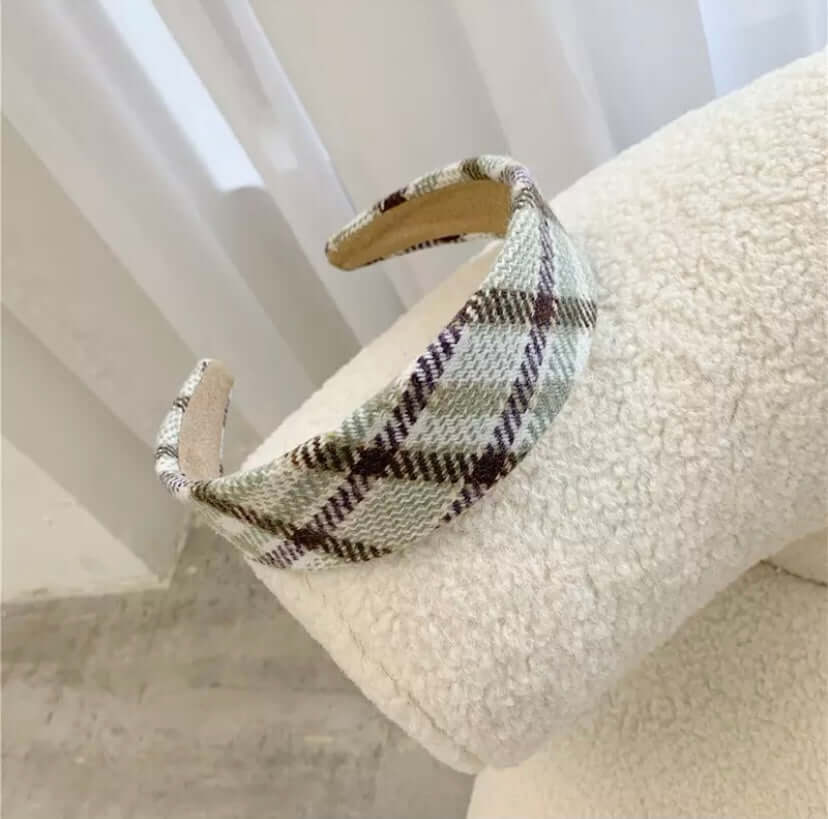 A single mint green and dark plaid padded headband resting on a cream boucle chair.