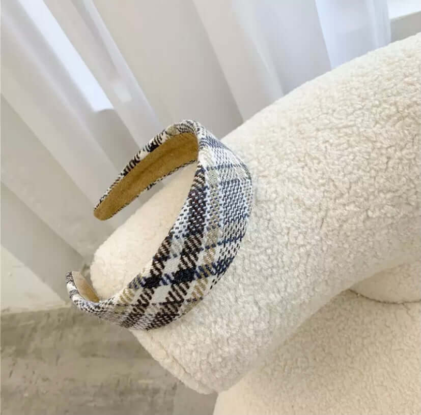 A single black, white and tan plaid padded headband resting on a cream boucle chair.
