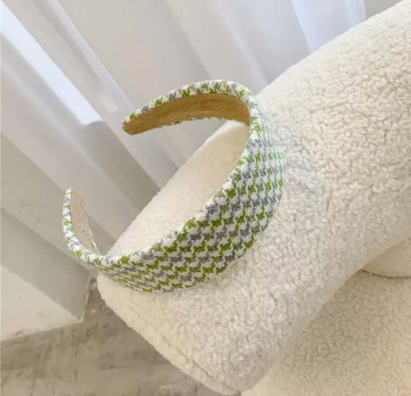 A single green, grey and cream houndstooth check padded headband resting on a cream boucle chair.