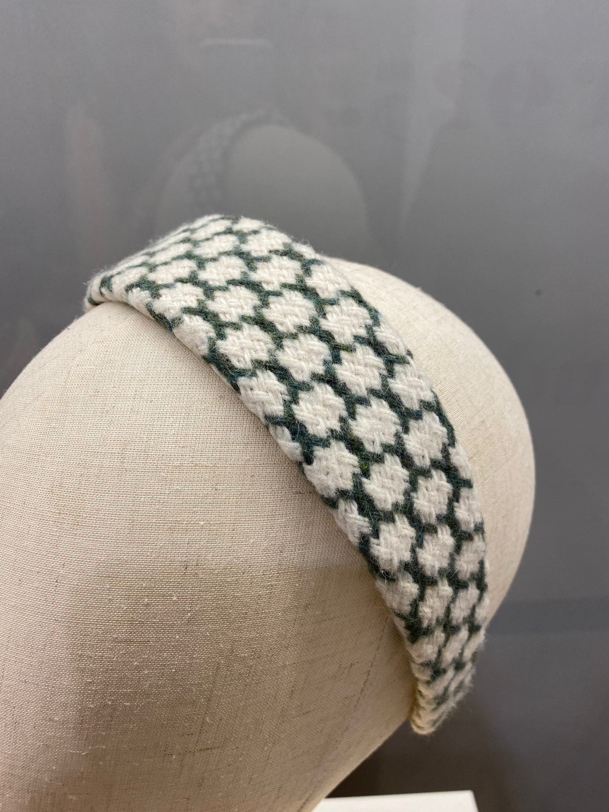 A single dark green and cream houndstooth check padded headband on a mannequin head, studio shot.