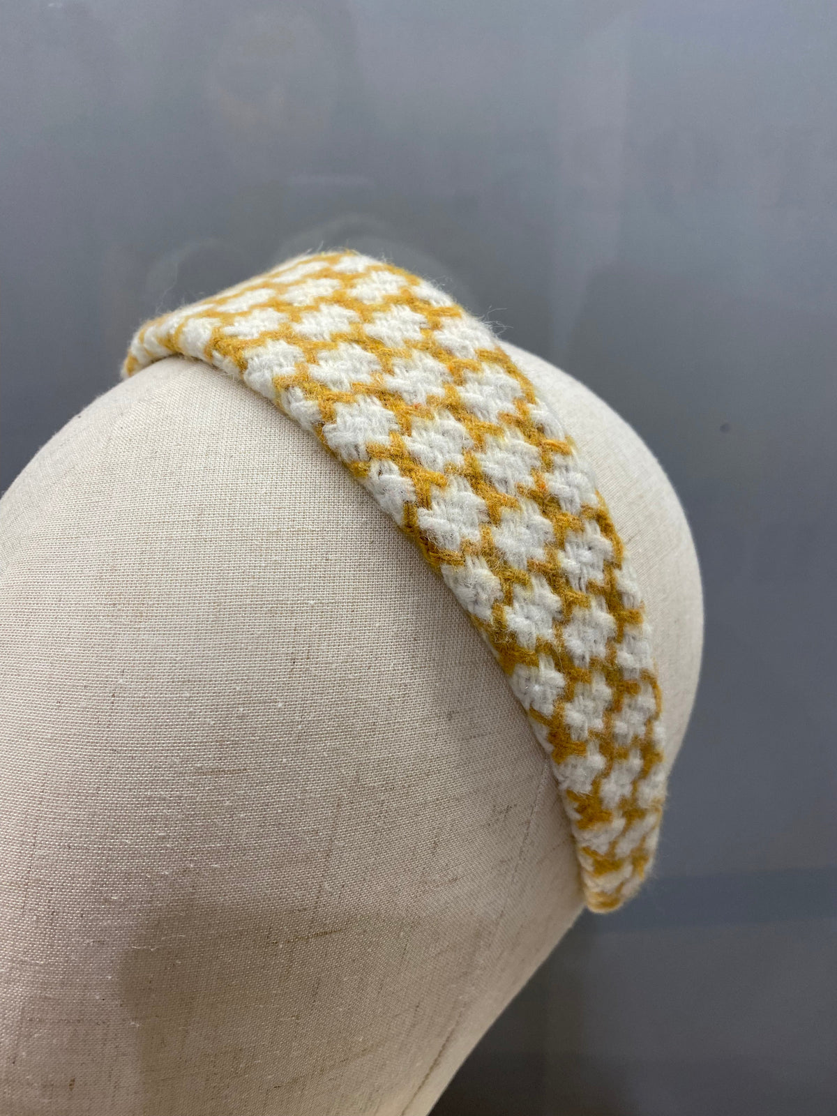 A single mustard and cream houndstooth check padded headband on a mannequin head, studio shot.