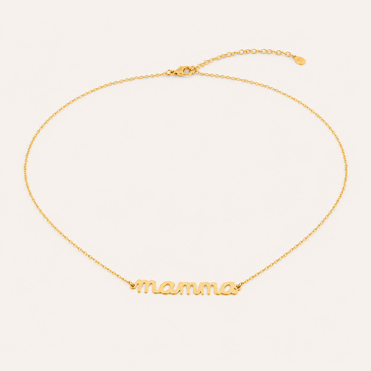 The Mama Big NECKLACE in gold, a script mamma pendant on a fine chain with a lobster clasp, shown on a cream background.