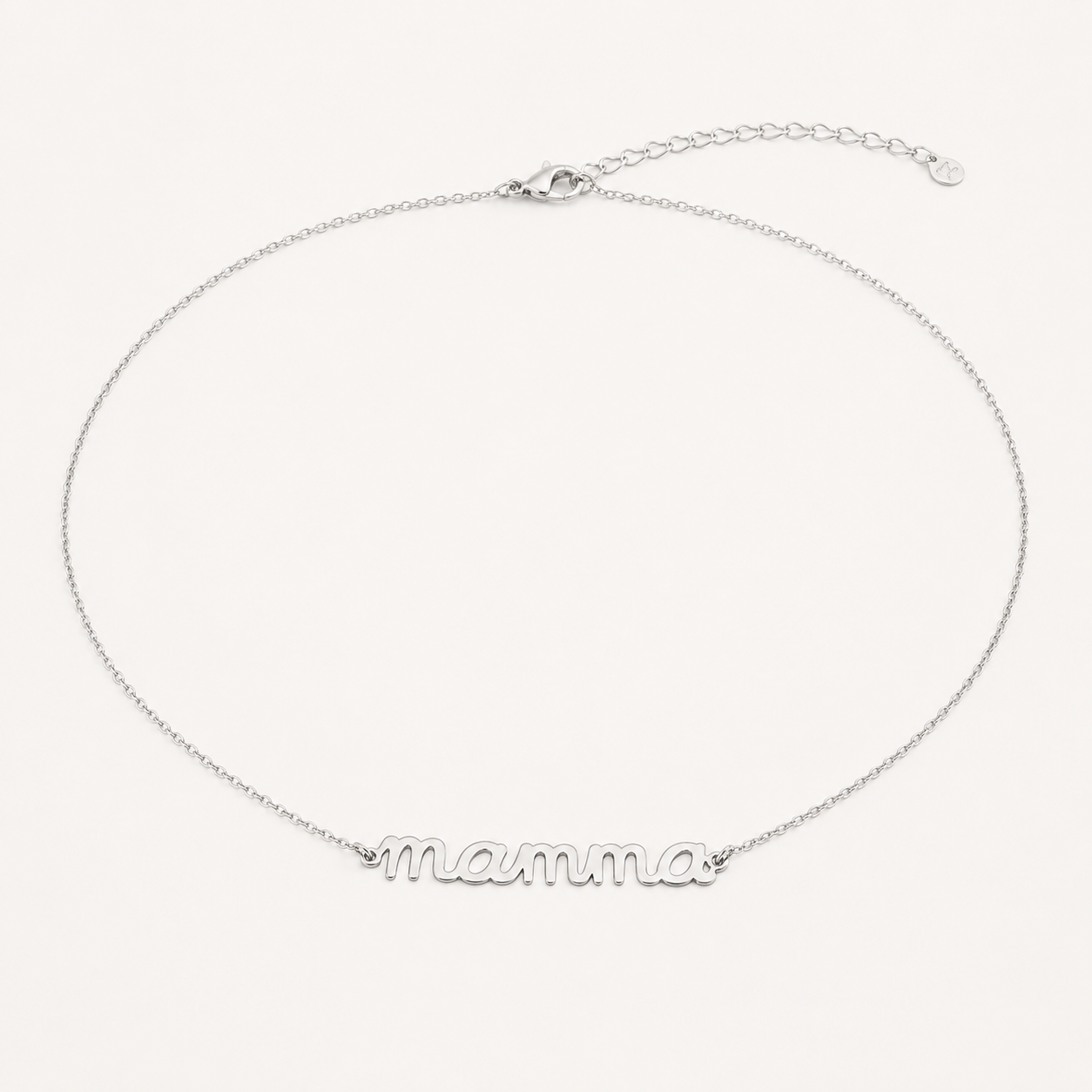 The Mama Big NECKLACE in silver, a script mamma pendant on a fine chain with a lobster clasp, shown on a cream background.