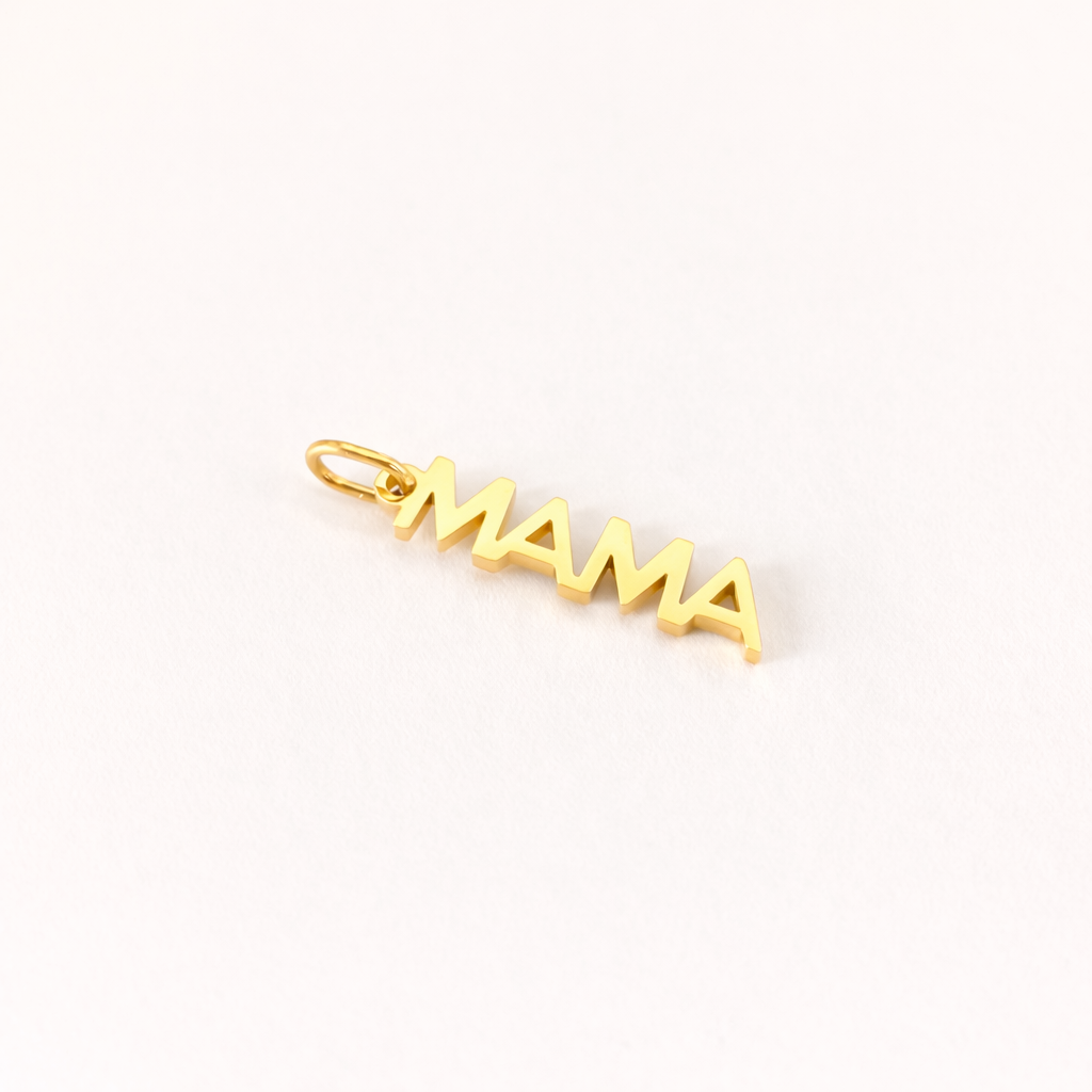 The Mama CHARM in a close-up flat lay, a gold vertical script pendant reading MAMA shown at an angle on cream fabric.
