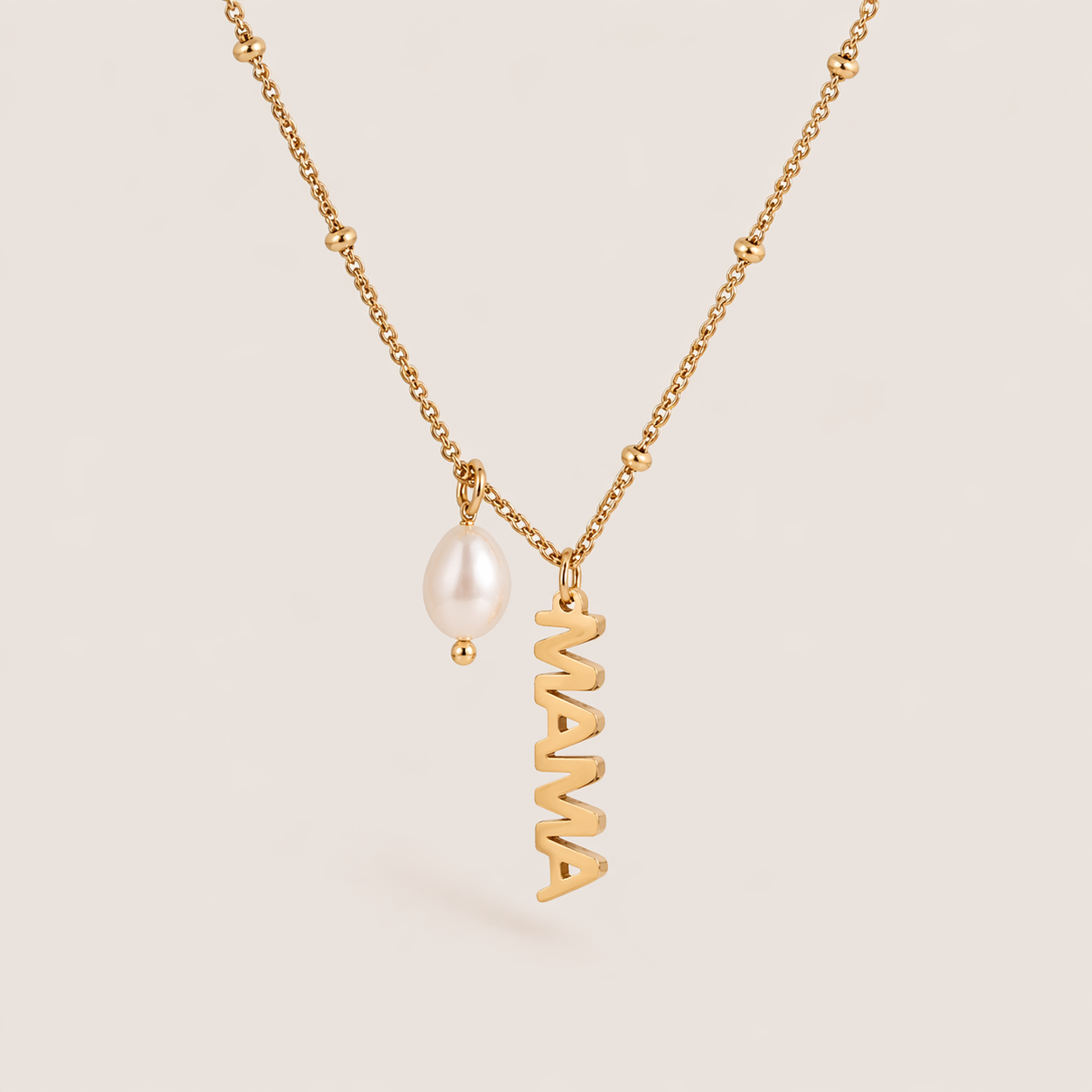 The Mama Pearl NECKLACE laid flat, showing a gold satellite chain with a dangling freshwater pearl beside a vertical MAMA script charm.